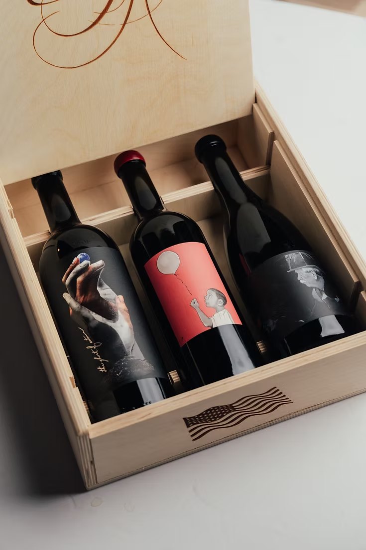 An open wooden three-bottle box holding all three releases, an American flag engraved into the front panel.